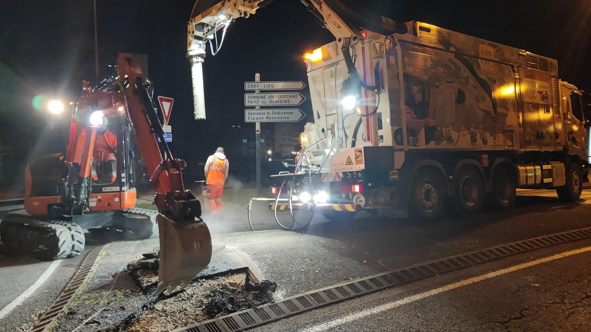 Chantier de nuit éclairé : camion aspiratrice-excavatrice AIX TP et mini-pelle en intervention sur chaussée